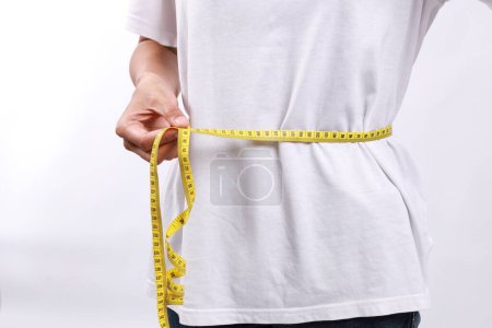 Mujer de cerca con camisa azul midiendo su cintura con cinta métrica amarilla. Pérdida de peso, cuerpo delgado, concepto de estilo de vida saludable. Figura de control y conteo de calorías. Plan de dieta exitosa.