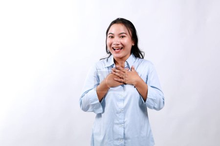 Bild einer überraschten und dankbaren jungen Frau, die ein Geschenk entgegennimmt, die Hände auf der Brust hält, mit geschmeicheltem Lächeln Danke sagt, gelobt wird, vor weißem Hintergrund steht.