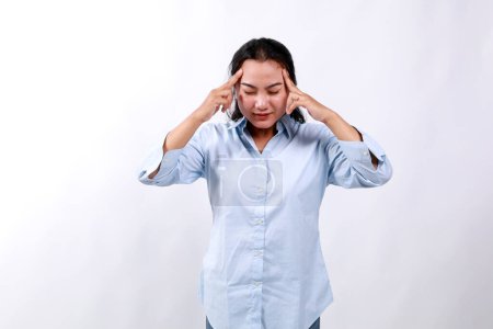 Frustrierte asiatische Frau, berührt ihren Kopf, zeigt auf die Stirn, steht mit geschlossenen Augen und besorgtem Gesicht, hat Kopfschmerzen, denkt nach, versucht sich zu erinnern. Isoliert auf weißem Hintergrund.
