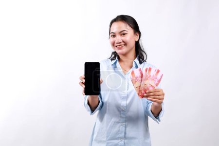 Mujer asiática mostrando la pantalla del teléfono móvil y dinero en efectivo, dinero, concepto de microcrédito y préstamos bancarios, de pie sobre fondo blanco