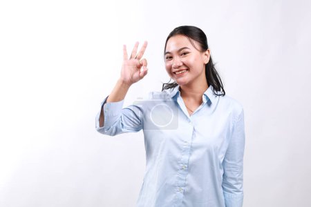 Lächelnde asiatische Frau zeigt Okay, Sehr gut mit zufriedenem Gesichtsausdruck, Lob und Kompliment großartige Arbeit, zufrieden mit etw, steht über weißem Hintergrund