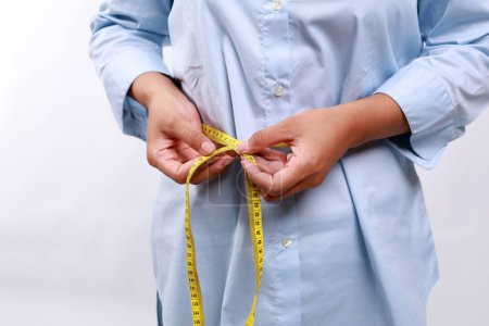 Mujer de cerca con camisa azul midiendo su cintura con cinta métrica amarilla. Pérdida de peso, cuerpo delgado, concepto de estilo de vida saludable. Figura de control y conteo de calorías. Plan de dieta exitosa.