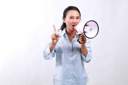 Strict woman of Asian ethnicity 20s wear blue shirt hold scream in megaphone announces warning, discounts sale Hurry up point finger up warns isolated on white background People lifestyle concept