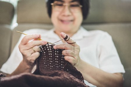 Photo for Handmade hobby stay home concept, Happy asian old woman knit brown scarf crochet on sofa in living room at home - Royalty Free Image