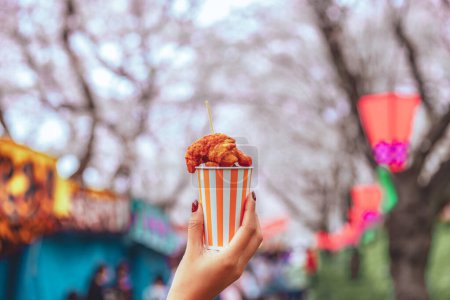 Téléchargez les photos : Karaage frit poulet snack dans une tasse sur asiatique femme main avec sakura fleurs de cerisier festival fond à Tokyo, Japon, concept japonais street food - en image libre de droit