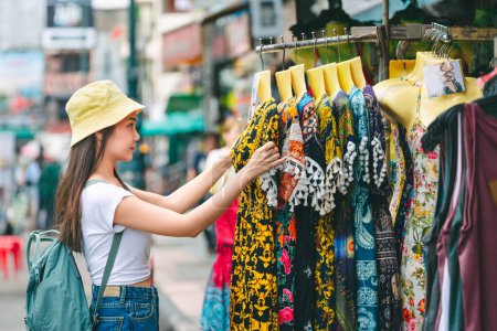 Photo for Lifestyle travel shopping concept, Young happy traveler asian woman with backpack and hat choosing cloth in shop store on shopping street outdoor market at Khaosan Road in Bangkok, Thailand - Royalty Free Image