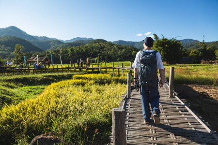 Téléchargez les photos : Voyage solo relaxer concept de vacances, Jeune voyageur asiatique heureux et photographe homme avec appareil photo et sac à dos visites sur le pont de bambou avec rizière à la ferme à Boon Kho Koo So, Chiang Mai, Thaïlande - en image libre de droit