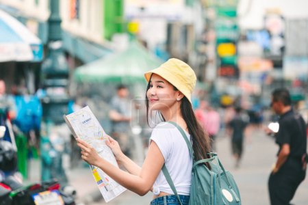 Foto de Viajes concepto de ciudad de vacaciones, joven viajero feliz mujer asiática con mapa y mochila caminando en Khaosan Road mercado al aire libre en Bangkok, Tailandia - Imagen libre de derechos