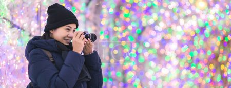Photo for Travel winter concept, Traveler asian woman or photographer taking photo with backpack and camera against light up bokeh background in winter illumination festival at Hokkaido, Japan - Royalty Free Image