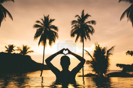 Photo for Summer travel vacation concept, Silhouette happy traveler asian woman relax and making hand on heart shape in infinity pool at resort with beach background at sunset in Koh Kood, Thailand - Royalty Free Image