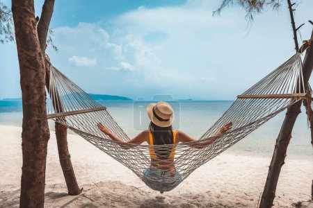 Téléchargez les photos : Voyage d'été concept de vacances, Heureux voyageur asiatique femme avec chapeau se détendre dans hamac sur la plage à Koh Rap, Samui, Surat Thani, Thaïlande - en image libre de droit