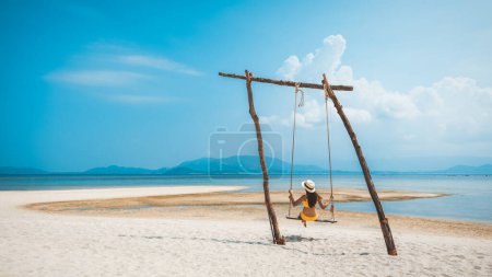Téléchargez les photos : Voyage d'été concept de vacances, Heureux voyageur asiatique femme avec bikini et chapeau se détendre dans swing sur la plage à Koh Rap, Samui, Surat Thani, Thaïlande - en image libre de droit