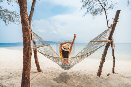 Téléchargez les photos : Voyage d'été concept de vacances, Heureux voyageur asiatique femme avec chapeau se détendre dans hamac sur la plage à Koh Rap, Samui, Surat Thani, Thaïlande - en image libre de droit