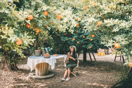 Téléchargez les photos : Heureux voyageur asiatique femme avec Ice café tasse en plastique tenant la main se détendre et Voyage dans le café jardin orange à la Thaïlande - en image libre de droit