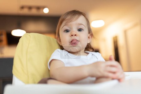 Photo for Adorable one year old child sitting in the highchair sticking out its tongue, shallow depth of field - Royalty Free Image