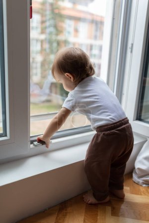 Téléchargez les photos : Portrait d'un adorable enfant d'un an regardant à travers la fenêtre, faible profondeur de champ - en image libre de droit