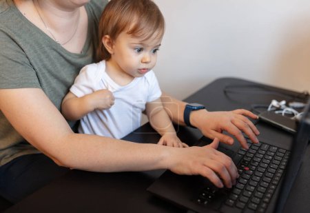 Téléchargez les photos : Mère qui travaille avec un enfant et un ordinateur portable au bureau à domicile - en image libre de droit