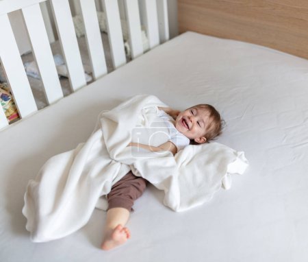 Foto de Adorable niño de 12 meses en la cama jugando con manta - Imagen libre de derechos