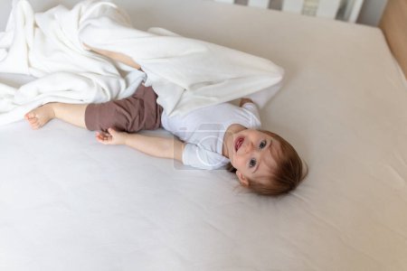 Téléchargez les photos : Adorable enfant de 12 mois au lit jouant avec la couverture - en image libre de droit