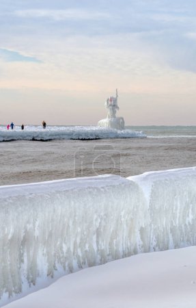 Tourists hike out carefully over a frozen boardwalk, to see the ice covered light beacon in St Joseph MI USA