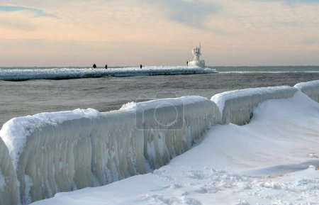 tourists walk out to see the frozen light beacon on north pier and to marvel at the frozen icy sculpture everything has become