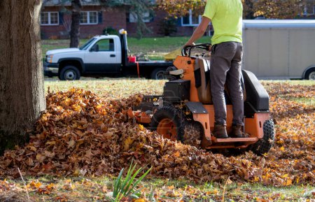 Ein Arbeiter benutzt eine Rasenlaubmaschine, um Laub zu mulchen und Haufen auf einem Hof aufzuräumen