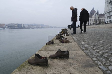 Foto de Tourist visit the memorial of shoes remembering the Holocaust victims on the bank of the River Danube in downtown Budapest, Hungary on December 22, 2022. - Imagen libre de derechos