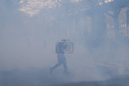 Téléchargez les photos : Des manifestants masqués réagissent au milieu de gaz lacrymogènes lors d'affrontements avec la police anti-émeute à la fin d'une manifestation nationale à Paris, en France, le 6 avril 2023. - en image libre de droit