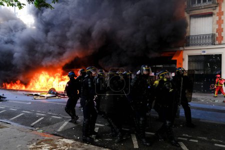 Foto de Oficiales de la policía antidisturbios francesa están cerca de un incendio en un edificio durante la marcha laboral del Primero de Mayo, un día de movilización contra la ley francesa de reforma de pensiones en París, Francia 1 de mayo de 2023. - Imagen libre de derechos