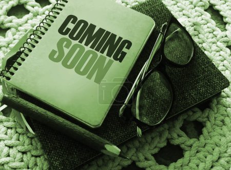 Coming soon on the cover of copybook, glasses and pen on crochet carpet. Business and education program concept.