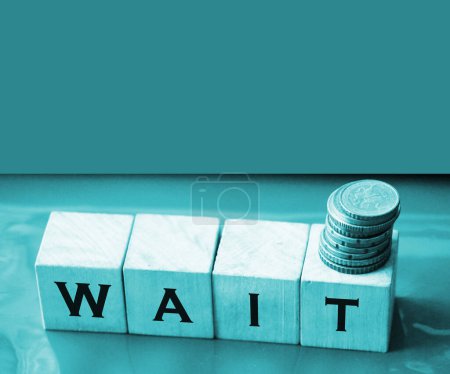 Wait text on a wooden cubes and coins. Business loan approval awaiting concept.