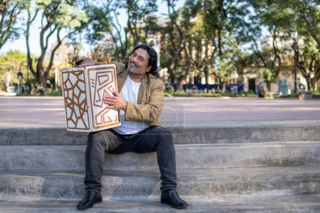 Foto de Músico hispano en un parque abrazando su caja de flamenco - Imagen libre de derechos