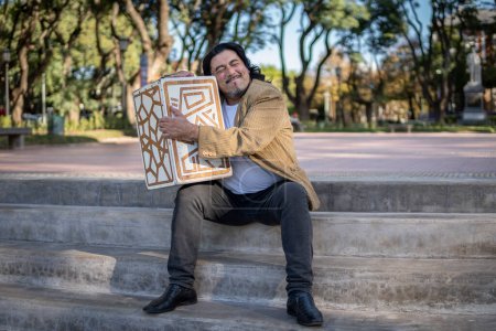 Foto de Músico hispano sentado en un parque abrazando su caja de flamenco - Imagen libre de derechos