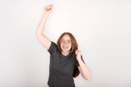 Photo for Portrait of young red haired woman celebrating, happy, with a winning expression, on pure background - Royalty Free Image