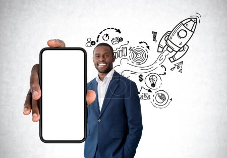 Téléchargez les photos : Homme d'affaires afro-américain souriant portant une tenue formelle tenant smartphone avec maquette près du mur de béton avec croquis en arrière-plan. Concept d'homme d'affaires, application mobile, start-up - en image libre de droit