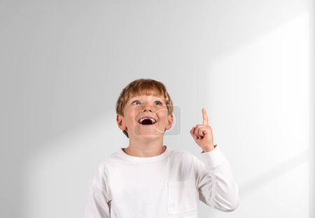 Foto de Niño de la escuela feliz con la boca abierta, retrato con el dedo apuntando hacia arriba en el espacio de copia fondo blanco. Concepto de salida y solución - Imagen libre de derechos