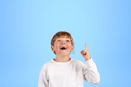 Foto de Niño inspirado en la escuela con la boca abierta y el dedo apuntando hacia arriba, retrato de niño inteligente en el espacio de copia fondo azul. Concepto de pregunta y solución - Imagen libre de derechos