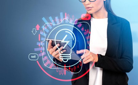 Photo for Businesswoman working with tablet, finer touch screen. Glowing light bulb hud hologram and candlesticks, rising price for energy and power. Concept of finance and economy - Royalty Free Image