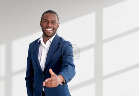Foto de Black happy businessman in blue formal suit, stretching out a hand to shake on copy space white background. Concept of partnership and business deal - Imagen libre de derechos