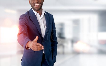Foto de Black happy businessman in blue formal suit, stretching out a hand to shake on copy space blurred office background. Concept of agreement and deal - Imagen libre de derechos