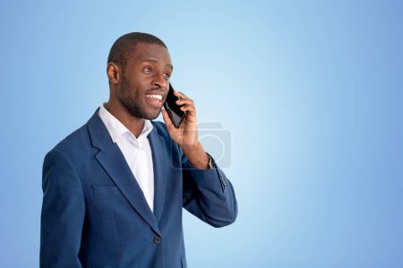 Foto de Smiling businessman calling on the phone, portrait in blue formal suit on copy space blue background. Concept of business connection and online network - Imagen libre de derechos