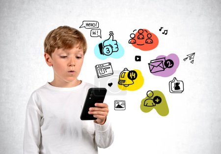 Foto de Pensive boy looking at phone in hand, colorful social media doodle icons on grey concrete background. Concept of online education and communication - Imagen libre de derechos