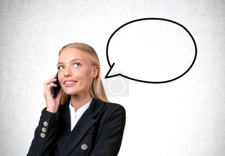 Foto de Attentive attractive businesswoman wearing formal wear standing talking on smartphone near concrete wall with speech bubble. Concept of ambitious business person, inspired woman, important call - Imagen libre de derechos