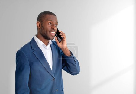 Foto de Smiling businessman calling on the phone, portrait in blue formal suit on copy space grey background. Concept of mobile connection and business network - Imagen libre de derechos