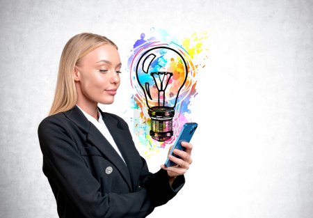 Foto de Happy businesswoman portrait profile using smartphone. Bright lightbulb doodle on grey concrete wall background. Concept of plan and startup - Imagen libre de derechos