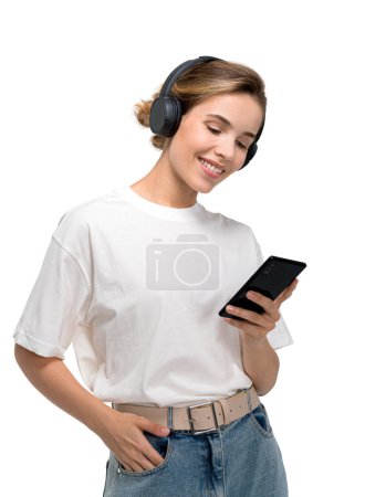 Téléchargez les photos : Smiling woman in white t-shirt using smartphone, wearing headphones. Isolated over white background. Concept for social media and music. - en image libre de droit