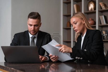 Photo for Two concentrated businessman and businesswoman working together with office documents, typing in laptop on desk in business room. Concept of teamwork and education - Royalty Free Image