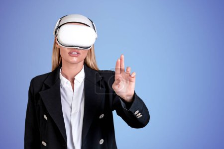 Photo for Businesswoman wearing vr headset is watching at metaverse reality. Empty blue wall in background. Concept of modern technology and progress in business, copy space, ambitious business person - Royalty Free Image