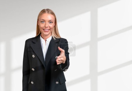 Téléchargez les photos : Smiling attractive businesswoman wearing formal wear standing stretching out hand for handshake near empty white wall in background. Concept of ambitious business person, inspired woman - en image libre de droit