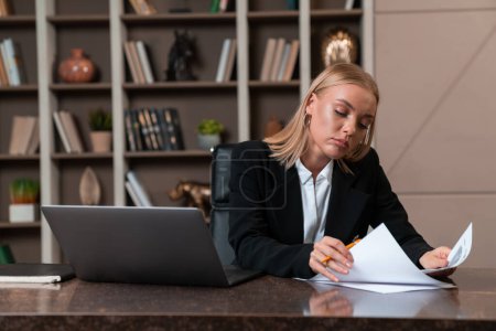 Foto de Thoughtful attractive businesswoman wearing formal wear sitting reading contract at office workplace in background. Concept of model, pondering business person, considered woman, information, lawyer - Imagen libre de derechos
